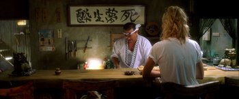 Movie still from “Kill Bill: Vol. 1” (2003), directed by Quentin Tarantino – A man standing in front of a table with food on top of it; Medium shot, Over the shoulder angle