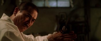 Movie still from “Kill Bill: Vol. 1” (2003), directed by Quentin Tarantino – A man in a white shirt is holding a black object; Close Up shot, Low angle