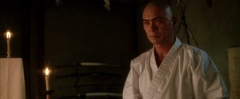 Movie still from “Kill Bill: Vol. 1” (2003), directed by Quentin Tarantino – A man in a white robe stands in front of a wall; Close Up shot, Low angle