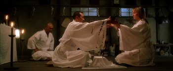Movie still from “Kill Bill: Vol. 1” (2003), directed by Quentin Tarantino – A man kneeling on the ground wearing a white robe; Wide shot, Low angle