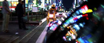 Movie still from “Kill Bill: Vol. 1” (2003), directed by Quentin Tarantino – A man riding a motorcycle down a street at night; Wide shot, Low angle