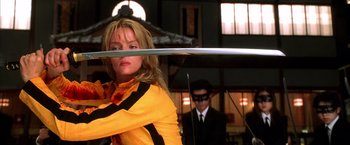 Movie still from “Kill Bill: Vol. 1” (2003), directed by Quentin Tarantino – A woman holding a sword in front of a man in a suit and tie; Medium shot, Low angle