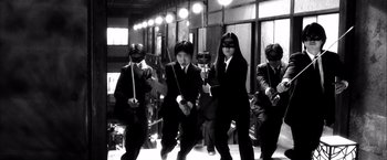 Movie still from “Kill Bill: Vol. 1” (2003), directed by Quentin Tarantino – A black and white photo of a group of people wearing masks; Medium shot, Low angle