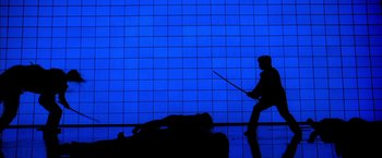 Movie still from “Kill Bill: Vol. 1” (2003), directed by Quentin Tarantino – A person holding a sword in front of a blue wall; Wide shot, Over the shoulder angle