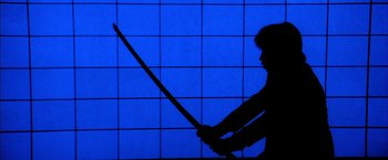 Movie still from “Kill Bill: Vol. 1” (2003), directed by Quentin Tarantino – A person holding a sword in front of a blue background; Wide shot, Low angle