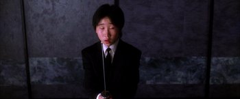 Movie still from “Kill Bill: Vol. 1” (2003), directed by Quentin Tarantino – A person in a black suit holding a drink; Close Up shot, Low angle