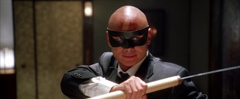 Movie still from “Kill Bill: Vol. 1” (2003), directed by Quentin Tarantino – A man in a suit and mask holding onto a rail; Close Up shot, Low angle