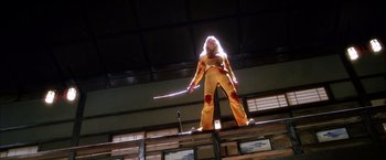 Movie still from “Kill Bill: Vol. 1” (2003), directed by Quentin Tarantino – A man in a yellow suit holding a sword in the dark; Wide shot, Low angle