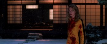 Movie still from “Kill Bill: Vol. 1” (2003), directed by Quentin Tarantino – A woman with blood on her body standing in front of a building; Medium shot, Over the shoulder angle