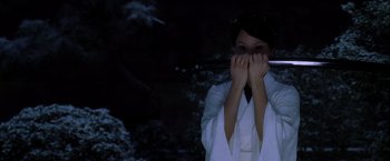 Movie still from “Kill Bill: Vol. 1” (2003), directed by Quentin Tarantino – A woman in a white robe holding a wooden stick; Close Up shot, Over the shoulder angle