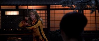 Movie still from “Kill Bill: Vol. 1” (2003), directed by Quentin Tarantino – A woman in a yellow and black jacket is in front of a building; Medium shot, Over the shoulder angle