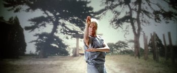 Movie still from “Kill Bill: Vol. 2” (2004), directed by Quentin Tarantino – A woman is doing an exercise in front of a tree; Medium shot, Low angle