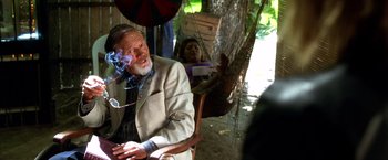 Movie still from “Kill Bill: Vol. 2” (2004), directed by Quentin Tarantino – An older man smoking a cigarette while sitting in a chair; Medium shot, Over the shoulder angle