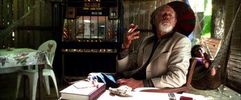 Movie still from “Kill Bill: Vol. 2” (2004), directed by Quentin Tarantino – An older man sitting at a table in front of an open book; Medium shot, Low angle