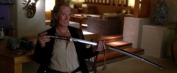 Movie still from “Kill Bill: Vol. 2” (2004), directed by Quentin Tarantino – A man holding a sword while sitting in a chair; Close Up shot, Over the shoulder angle
