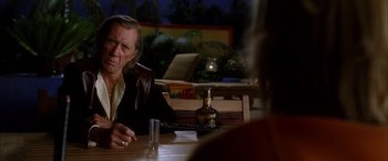 Movie still from “Kill Bill: Vol. 2” (2004), directed by Quentin Tarantino – A man sitting at a wooden table with a glass of whiskey; Medium shot, Over the shoulder angle