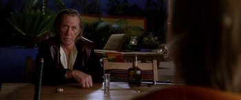 Movie still from “Kill Bill: Vol. 2” (2004), directed by Quentin Tarantino – An older man sitting at a table with a bottle of whiskey; Medium shot, Over the shoulder angle