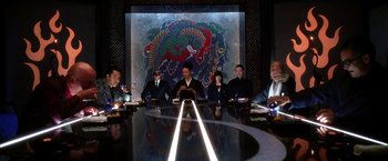 Movie still from “Kill Bill: Vol. 2” (2004), directed by Quentin Tarantino – A group of people sitting around a table in front of a painting; Wide shot, High angle