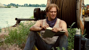 Movie still from “Kill the Irishman” (2011), directed by Jonathan Hensleigh – A man sitting on the ground holding a book; Medium shot, Low angle