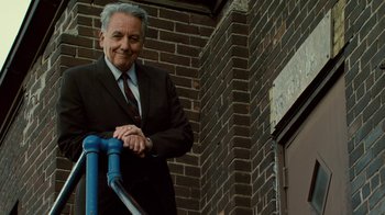 Movie still from “Kill the Irishman” (2011), directed by Jonathan Hensleigh – An older man in a suit and tie leaning on a blue pipe; Medium shot, Low angle