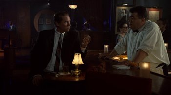 Movie still from “Kill the Irishman” (2011), directed by Jonathan Hensleigh – Two men sitting at a table in front of a lamp; Medium shot, Over the shoulder angle