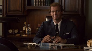 Movie still from “Kill the Irishman” (2011), directed by Jonathan Hensleigh – A man sitting at a desk in a suit and tie; Medium shot, Over the shoulder angle