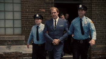 Movie still from “Kill the Irishman” (2011), directed by Jonathan Hensleigh – A man in a suit is being escorted by police officers; Medium shot, Low angle
