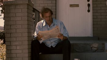 Movie still from “Kill the Irishman” (2011), directed by Jonathan Hensleigh – A man sitting on the steps of a house reading a newspaper; Medium shot, Low angle