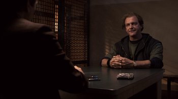 Movie still from “Kill the Irishman” (2011), directed by Jonathan Hensleigh – A man sitting at a table in front of a cell phone; Medium shot, Over the shoulder angle