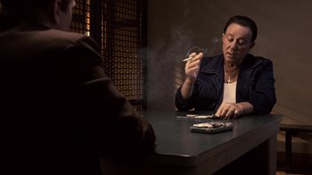 Movie still from “Kill the Irishman” (2011), directed by Jonathan Hensleigh – A woman sitting at a table smoking a cigarette; Medium shot, Over the shoulder angle