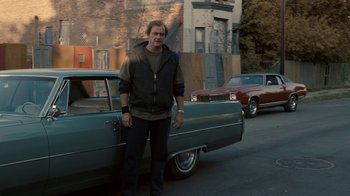 Movie still from “Kill the Irishman” (2011), directed by Jonathan Hensleigh – A man standing in front of a car on the side of the road; Wide shot, Over the shoulder angle