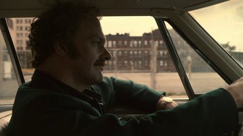 Movie still from “Kill the Irishman” (2011), directed by Jonathan Hensleigh – A man sitting in the driver's seat of a car looking out the window; Close Up shot, Over the shoulder angle