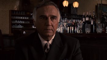 Movie still from “Kill the Irishman” (2011), directed by Jonathan Hensleigh – An older man wearing a suit and tie in front of a bar; Close Up shot, Over the shoulder angle