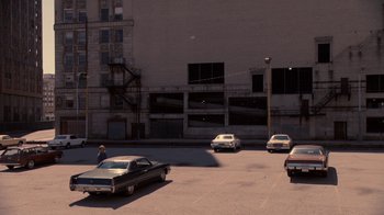 Movie still from “Kill the Irishman” (2011), directed by Jonathan Hensleigh – A man standing in a parking lot next to a row of parked cars; Extreme Wide shot, High angle
