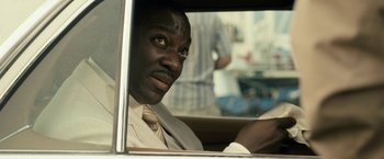 Movie still from “Killer Elite” (2011), directed by Gary McKendry – A man in a suit and tie driving a car; Close Up shot, Over the shoulder angle