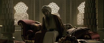 Movie still from “Killer Elite” (2011), directed by Gary McKendry – An old man sitting on a couch in front of a window; Medium shot, Low angle