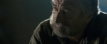 Movie still from “Killer Elite” (2011), directed by Gary McKendry – An older man with a beard and a mustache; Close Up shot, Over the shoulder angle
