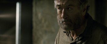 Movie still from “Killer Elite” (2011), directed by Gary McKendry – An older man with a beard and a mustache; Close Up shot, Over the shoulder angle