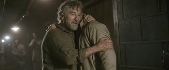 Movie still from “Killer Elite” (2011), directed by Gary McKendry – A man holding another man in his arms in a room; Medium shot, Over the shoulder angle