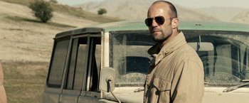 Movie still from “Killer Elite” (2011), directed by Gary McKendry – A man standing in front of an old truck; Close Up shot, Over the shoulder angle