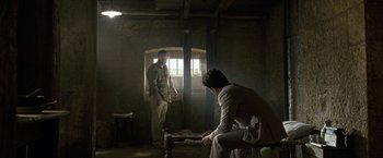 Movie still from “Killer Elite” (2011), directed by Gary McKendry – Two men standing in a dimly - lit room , one of them playing chess; Wide shot, Over the shoulder angle