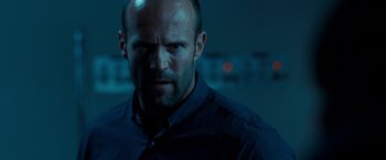 Movie still from “Killer Elite” (2011), directed by Gary McKendry – A man with a beard is looking at the camera; Close Up shot, Low angle