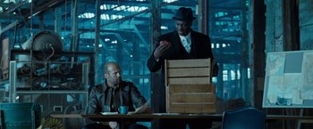 Movie still from “Killer Elite” (2011), directed by Gary McKendry – Two men sitting at a table with a box; Medium shot, Over the shoulder angle