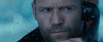 Movie still from “Killer Elite” (2011), directed by Gary McKendry – A man with a beard looking at the camera; Close Up shot, Over the shoulder angle