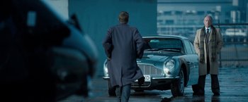 Movie still from “Killer Elite” (2011), directed by Gary McKendry – A man walking down a street next to a car; Wide shot, Over the shoulder angle