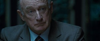 Movie still from “Killer Elite” (2011), directed by Gary McKendry – An older man wearing a suit and tie; Close Up shot, Over the shoulder angle