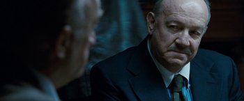 Movie still from “Killer Elite” (2011), directed by Gary McKendry – A man wearing a suit and tie sitting next to another man wearing a suit and tie; Close Up shot, Over the shoulder angle