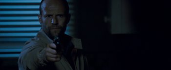 Movie still from “Killer Elite” (2011), directed by Gary McKendry – A man holding a gun while standing in the dark; Close Up shot, Low angle