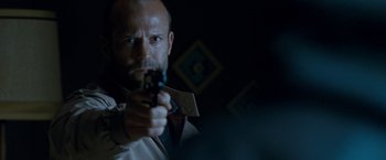 Movie still from “Killer Elite” (2011), directed by Gary McKendry – A man holding a gun while wearing a tie; Close Up shot, Low angle