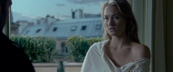 Movie still from “Killer Elite” (2011), directed by Gary McKendry – A woman standing in front of a building with trees in the background; Close Up shot, Over the shoulder angle